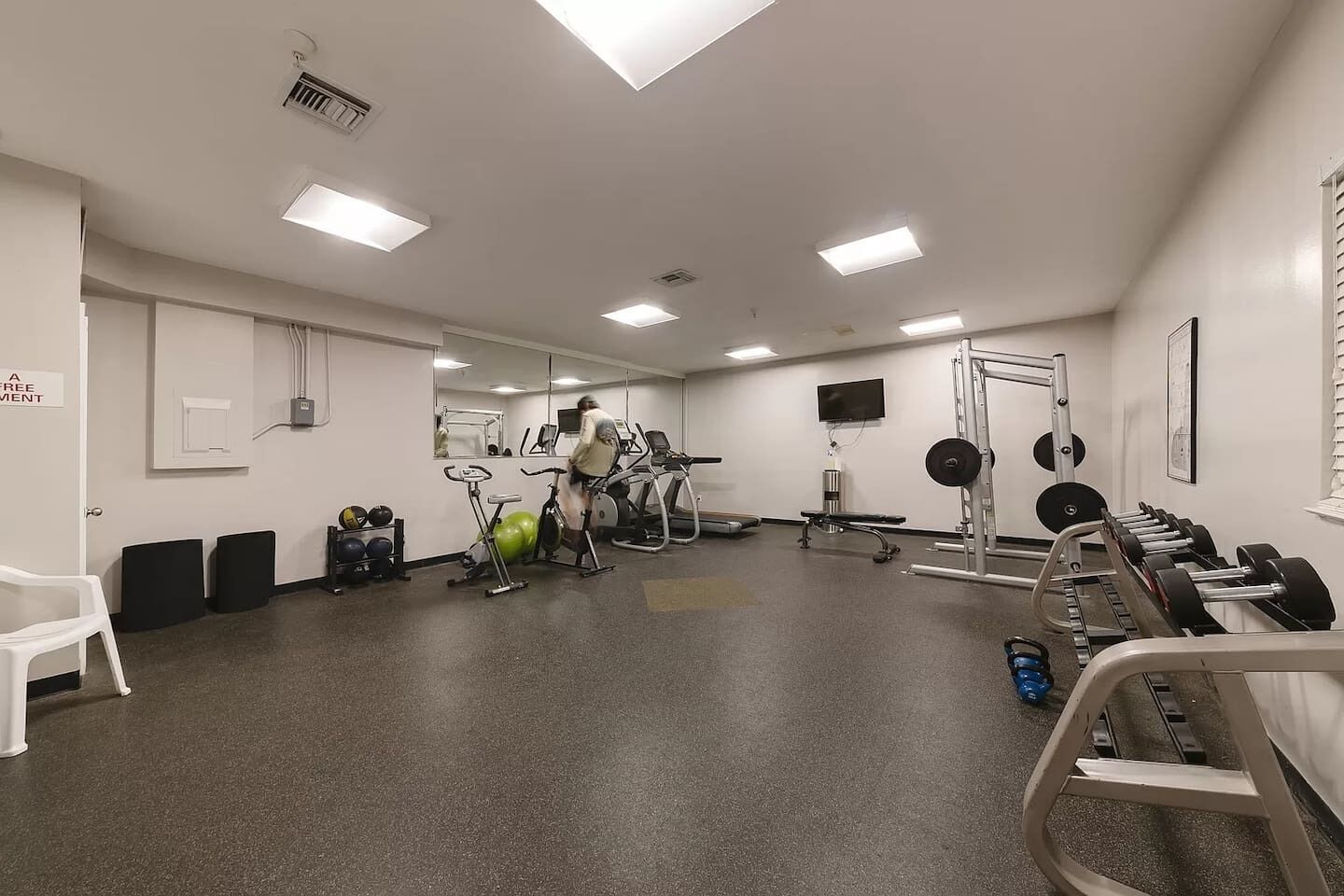 A gym with exercise equipment, a mirror, and a TV on the wall.