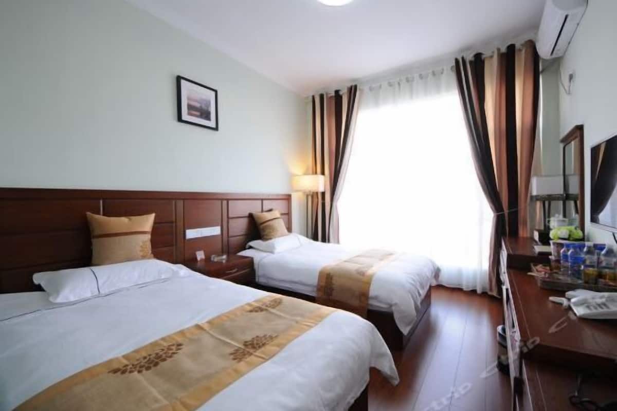 Habitación de hotel con dos camas, un escritorio con silla, un espejo y una ventana con cortinas.