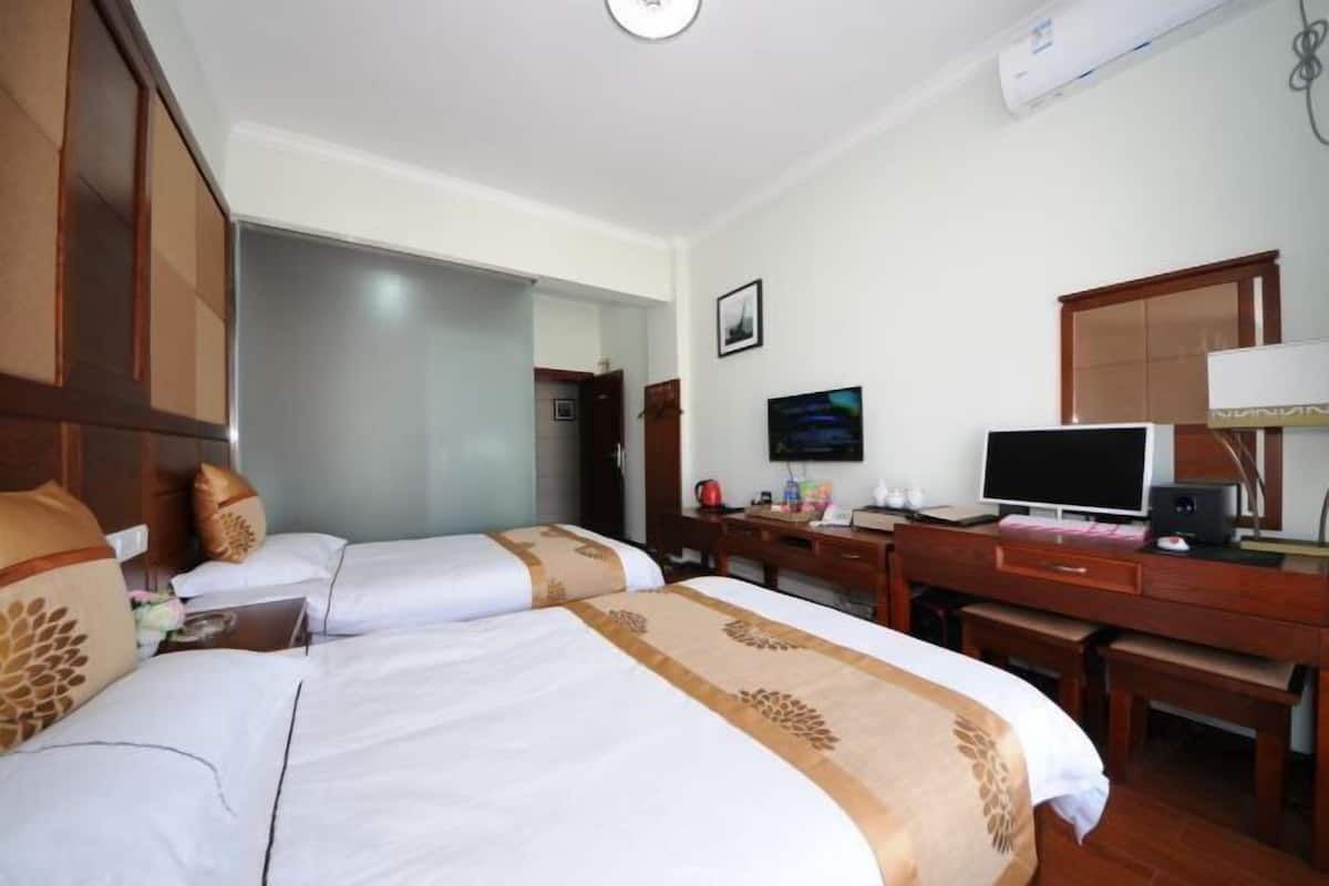 Habitación de hotel con dos camas, un escritorio con computadora, televisor y espejo.