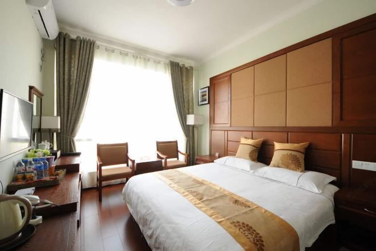 Una habitación de hotel con una cama grande, un escritorio con silla, un televisor y una ventana con cortinas.