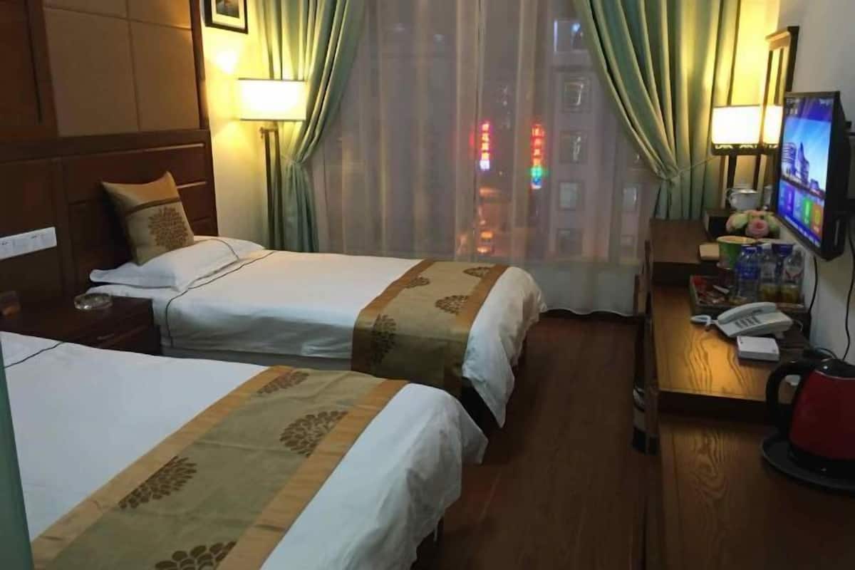 Habitación de hotel con dos camas, un escritorio con teléfono y hervidor, y un televisor en la pared.