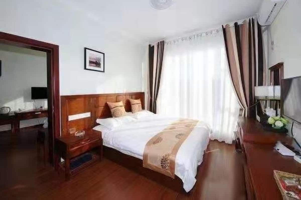 Habitación de hotel con una cama de madera, un escritorio con una silla, un espejo y una ventana con cortinas.