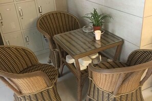 Een rieten eethoek met een tafel en vier stoelen, een bloempot en een wandkast.