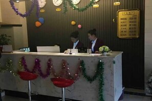 A reception desk with two staff members, a bulletin board, and a potted plant.