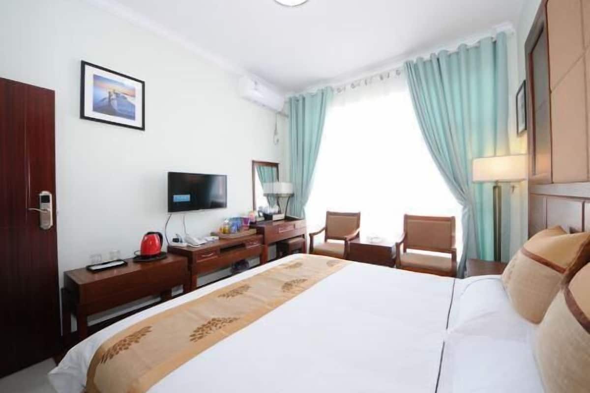 Habitación de hotel con cama, escritorio, televisor, silla y ventana con cortinas.