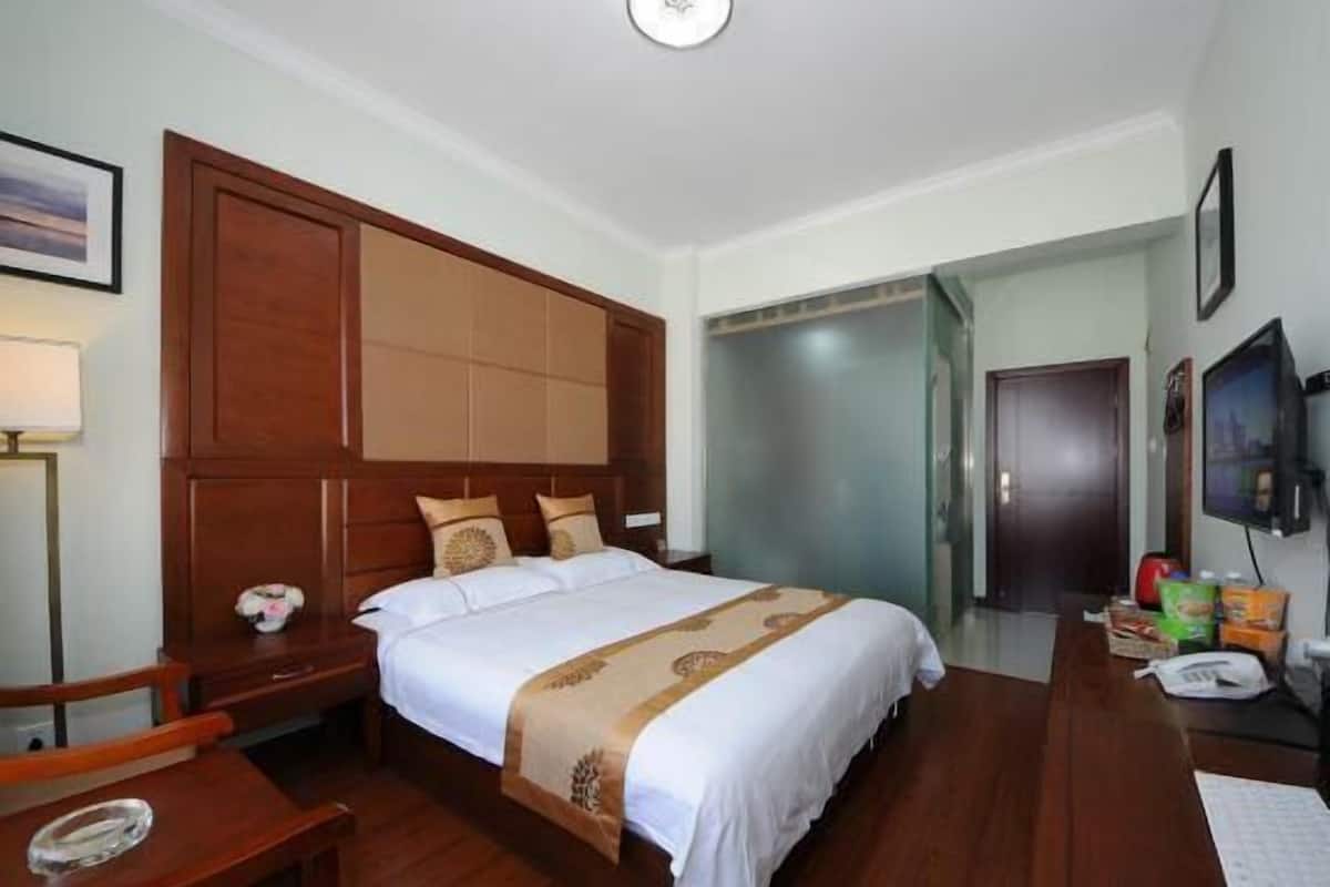 Habitación de hotel con una cama grande, cabecera de madera, un escritorio con silla, televisión y armario.