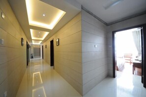 A hotel corridor with a modern design, featuring a long hallway with a glossy floor, recessed lighting, and a view into a room with a bed and a window.