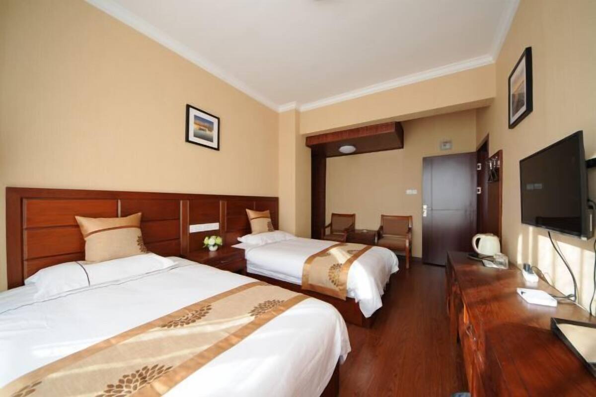Habitación de hotel con dos camas, cabecera de madera, escritorio con silla, televisor y puerta que da a otra habitación.