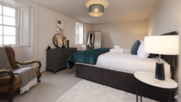A bedroom with a bed, a chair, a dresser, a mirror, and a lamp. - Observatory Apartment at Calton Hill (Edinburgh)