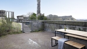 An outdoor patio with a table and benches, overlooking a historic tower and ruins. - Observatory Apartment at Calton Hill (Edinburgh)