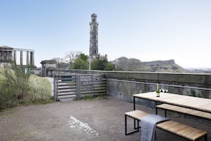 An outdoor patio with a table and benches, overlooking a historic tower and ruins.