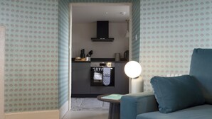 A modern living room with a blue sofa and a round table with a lamp. A kitchen is visible in the background with a stove and oven. - Observatory Apartment at Calton Hill (Edinburgh)