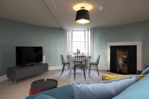 A living room with a TV, dining table, chairs, and a fireplace. - Observatory Apartment at Calton Hill (Edinburgh)