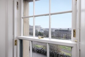 A view through a window with a stone wall and a building in the background. - Observatory Apartment at Calton Hill (Edinburgh)