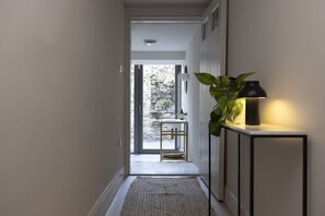 A hallway with a plant, a lamp, and a view of an outdoor area with a stone wall and a window. - Observatory Apartment at Calton Hill (Edinburgh)