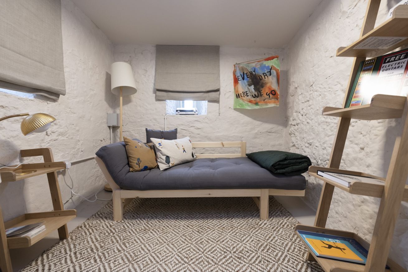 Une petite pièce agréable et chaleureuse, avec un lit simple, une lampe, une bibliothèque et une affiche accrochée au mur.