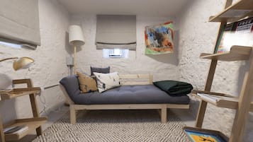 Une petite pièce agréable et chaleureuse, avec un lit simple, une lampe, une bibliothèque et une affiche accrochée au mur.