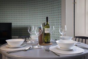 A dining table set with white bowls, plates, cutlery, and wine glasses, with a bottle of wine and a thermos on the table. - Observatory Apartment at Calton Hill (Edinburgh)