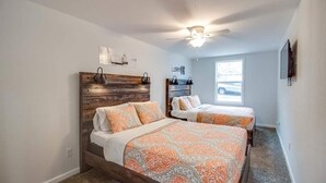 Une chambre avec deux lits, une tête de lit en bois, un ventilateur de plafond et une fenêtre donnant sur un véhicule à l’extérieur.