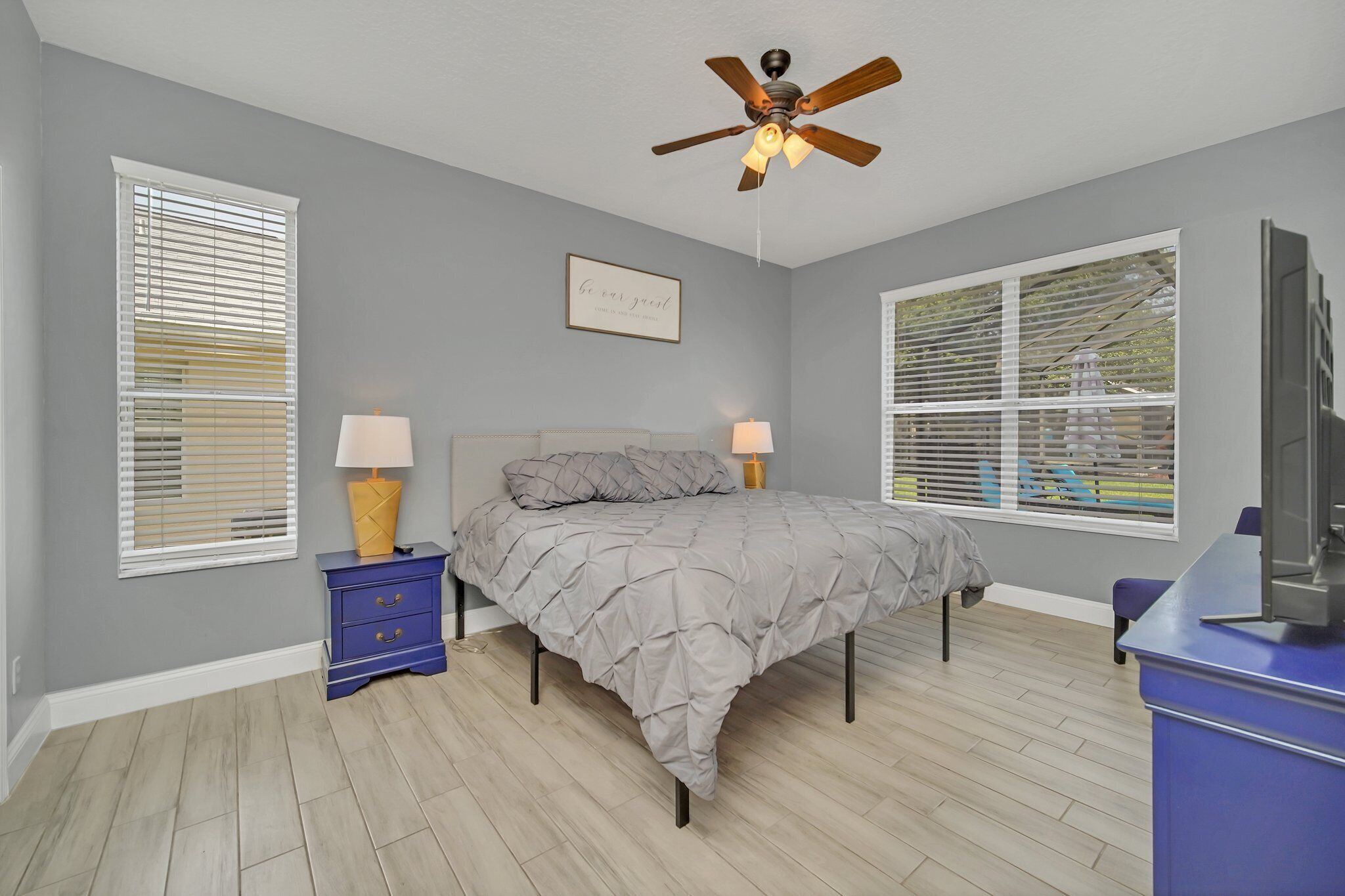 A bedroom with a bed, two bedside tables with lamps, a ceiling fan, and a TV.