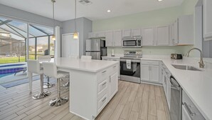 Una cocina moderna con armarios blancos, electrodomésticos de acero inoxidable y una isla grande con taburetes de bar.