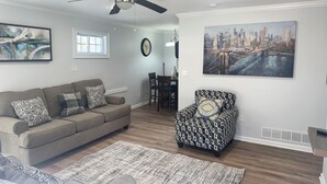 A living room with a grey sofa, patterned armchair, and a cityscape painting. - Chill & Relax 3bd (Marietta)