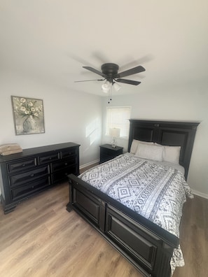 A bedroom with a bed, dresser, nightstands, a ceiling fan, a window with blinds, and a wall-mounted artwork. - Chill & Relax 3bd (Marietta)