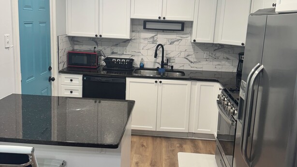 A kitchen with white cabinets, a black countertop, a stainless steel refrigerator, and a microwave. - Chill & Relax 3bd (Marietta)