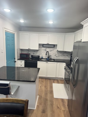 A kitchen with white cabinets, a black countertop, a stainless steel refrigerator, and a microwave. - Chill & Relax 3bd (Marietta)