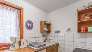 A kitchen with wooden cabinets, a Bosch dishwasher, a sink, a stove, and a window with lace curtains. - Chalet Bossons  - Welkeys (Chamonix-Mont-Blanc)