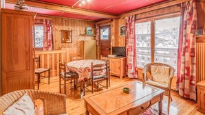 A cozy wooden cabin interior with a dining table, chairs, a sofa, and a television. - Chalet Bossons  - Welkeys (Chamonix-Mont-Blanc)