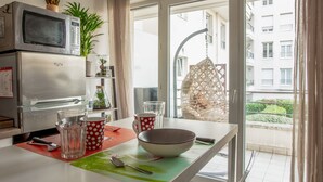 Una cocina con microondas, horno y vistas a un balcón con una silla colgante.