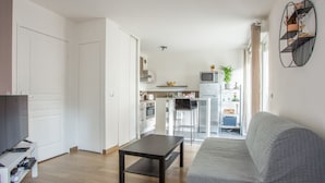 Una sala de estar moderna con un sofá gris, una mesa de centro de madera oscura y una cocina al fondo.
