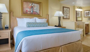 Une chambre d’hôtel avec un grand lit, deux tables de chevet, une petite table, une commode et une salle de bain.