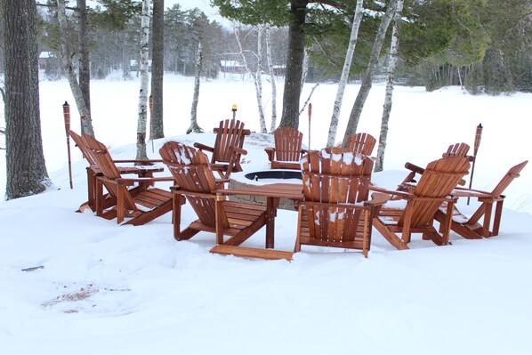 Un espace extérieur aménagé avec des meubles en bois, comprenant des chaises et une table centrale, le tout entouré de neige et d’arbres.