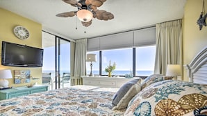 A bedroom with a large bed, a ceiling fan, a flat-screen TV, a window with curtains, and a view of the ocean. - Ocean Views & Pool Access: Myrtle Beach Condo! (Myrtle Beach)