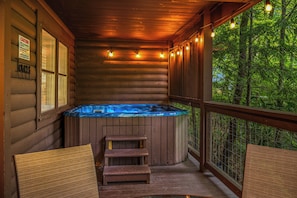 Relax in a hot tub on the deck overlooking a lush forest.