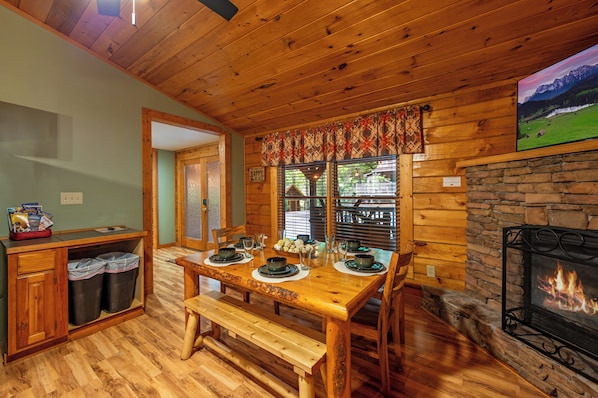 Enjoy meals in this cabin's dining area, featuring a wooden table, bench seating, and a stone fireplace.