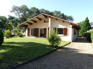 A two-story house with a sloped roof, wooden shutters, and a gravel driveway.