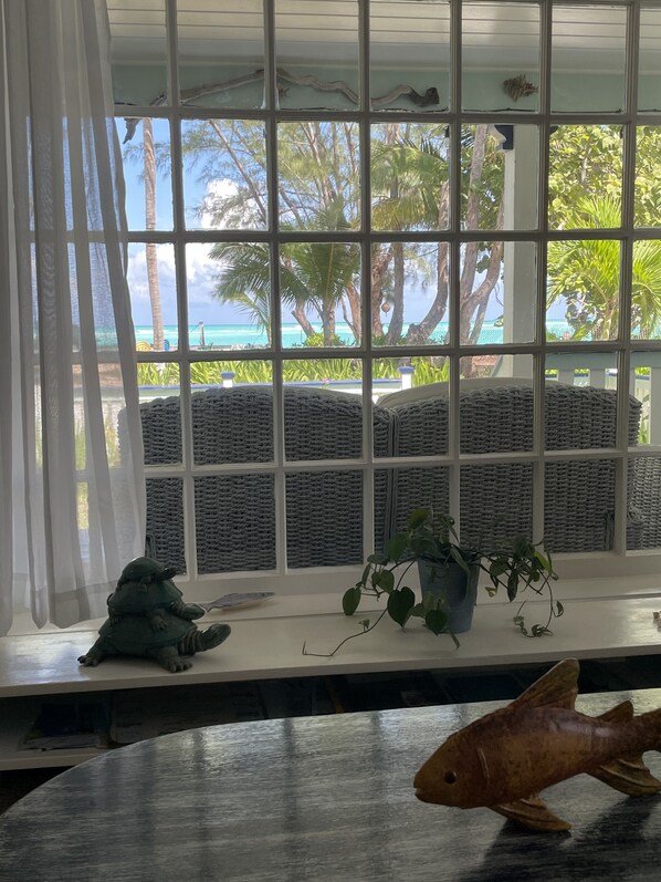 A room with a large window overlooking a beach, wicker furniture, and a small fish sculpture on the table. - Palmetto cottage on the beach with perfect views. (Spanish Wells)