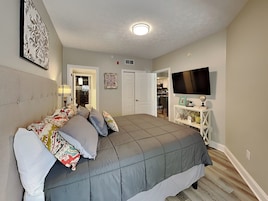 Un dormitorio con una cama grande, un televisor en la pared y una puerta que da a un baño.