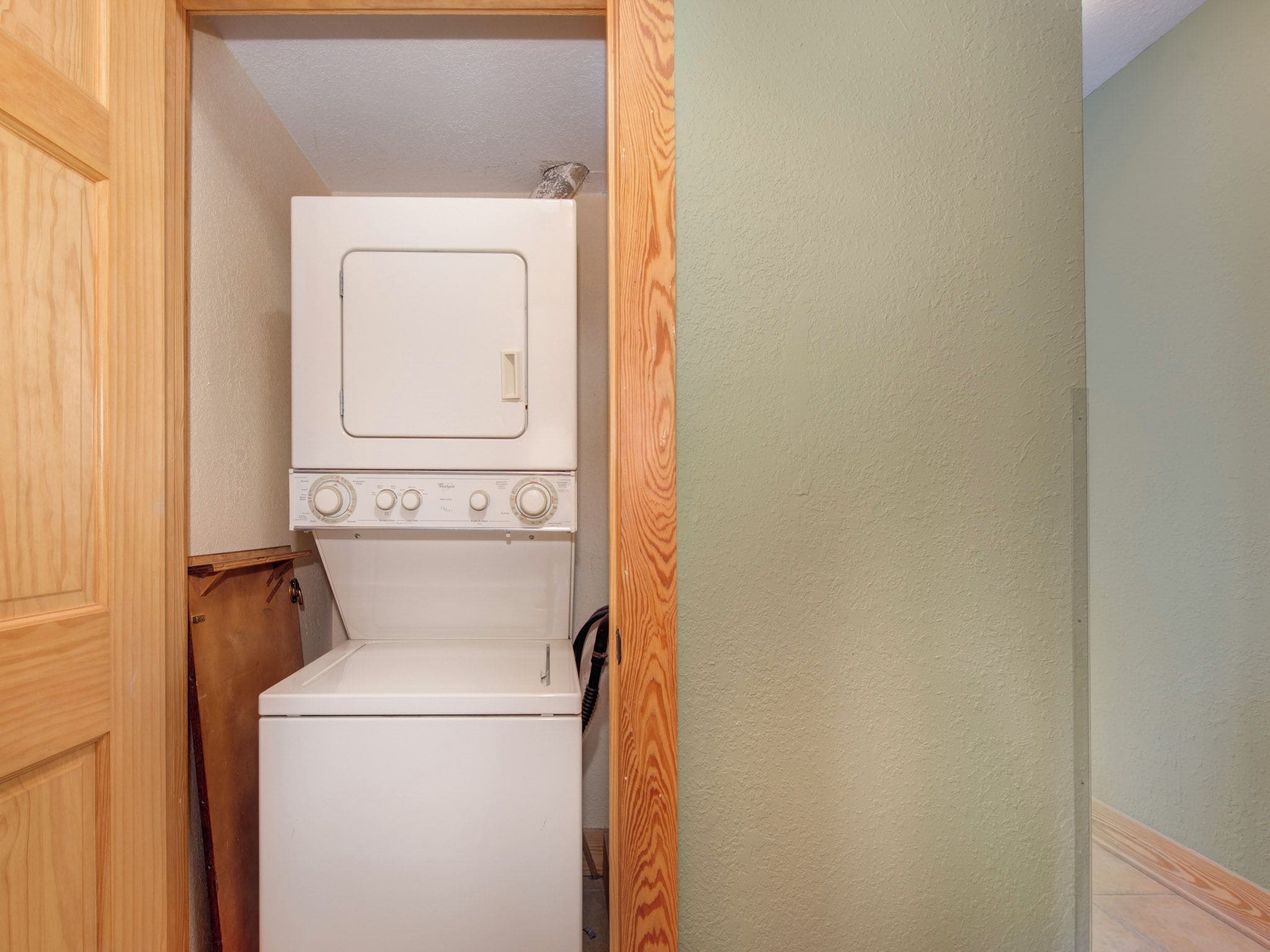 A compact laundry room with a front-loading washer and dryer, wooden cabinetry, and a plain wall.