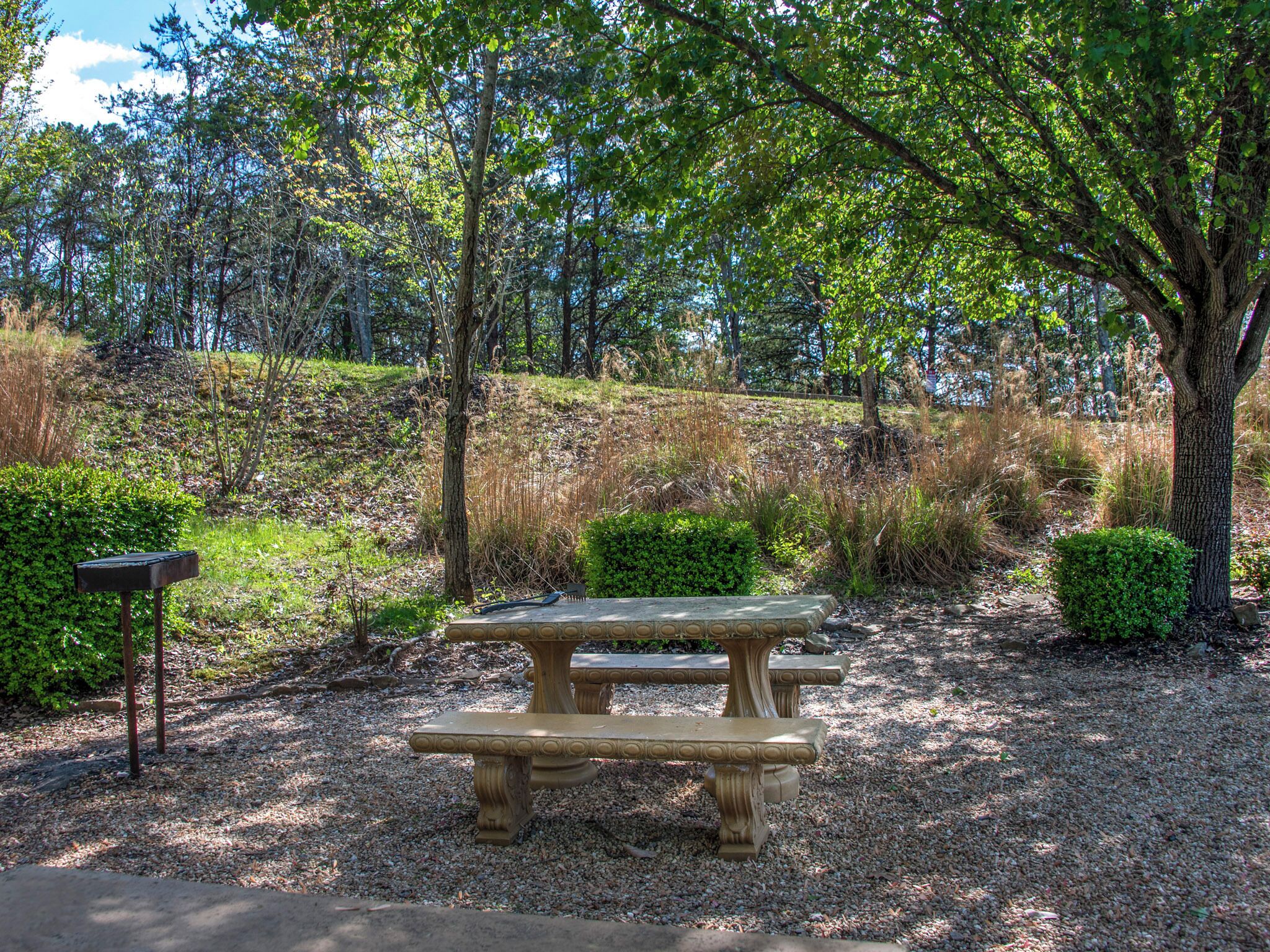 A picnic table in a park with a gravel ground, surrounded by trees and shrubs.