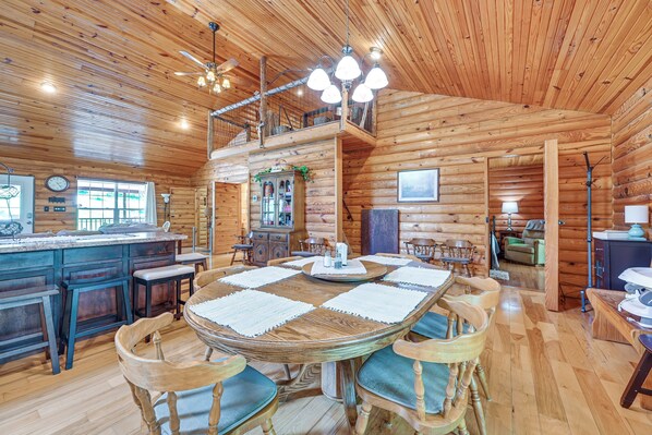 Cozy cabin-style interior with a central dining table, high ceiling, and kitchen area.