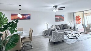 Un vaste espace de vie comprenant un canapé moderne, une table à manger avec des chaises et un ventilateur de plafond.