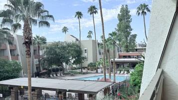 A pool area with palm trees, a barbecue setup, and a view of a building with balconies.