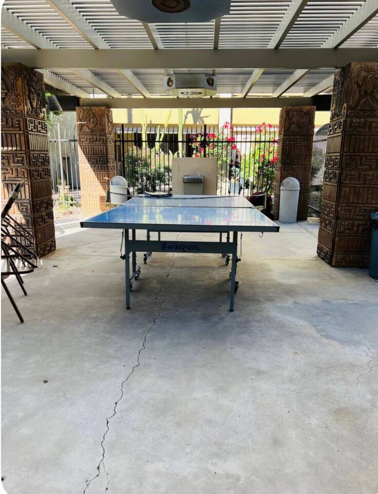 A ping pong table in an outdoor area with a ceiling fan, surrounded by brick pillars and metal railings.