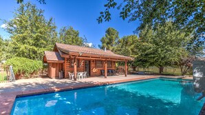 A wooden cabin with a pool, surrounded by trees and a fenced area.