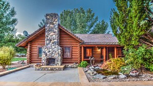 A log cabin with a stone chimney, a stone fireplace, and a well-maintained garden with a pond.