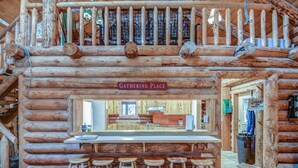 A log cabin with a bar area labeled "Gathering Place," featuring wooden stools and a kitchen visible through the entrance.